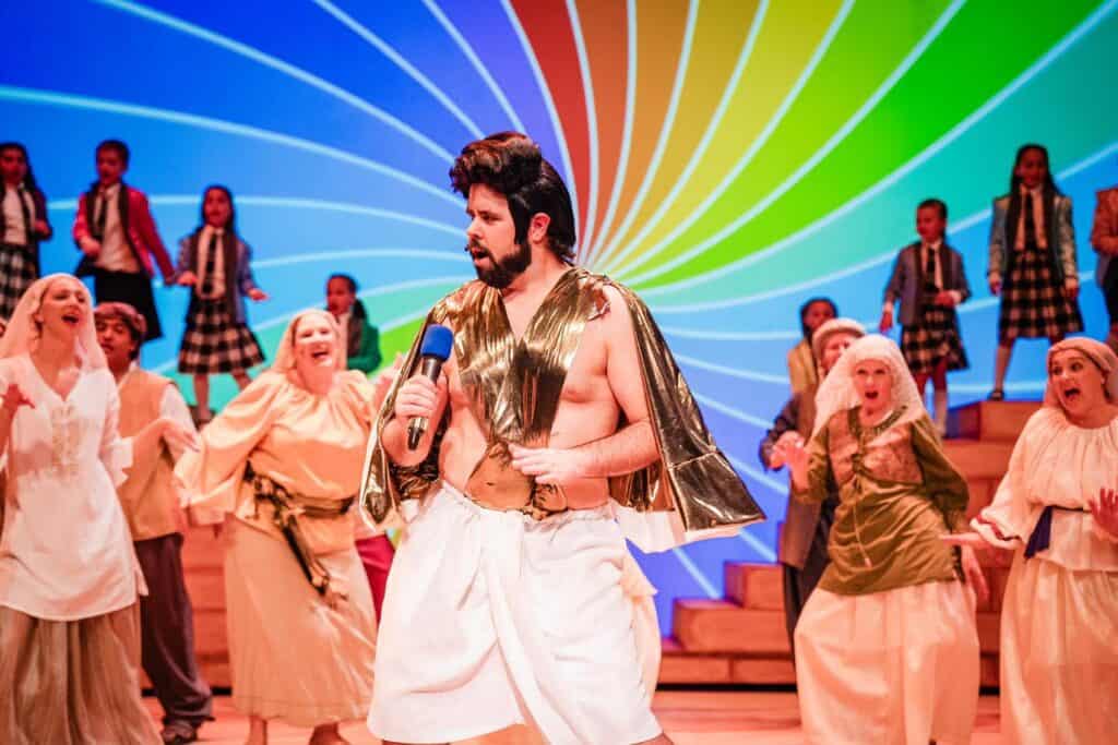 Vibrant theater performance at Oshawa Little Theatre featuring a diverse cast with dynamic stage lighting and colorful background.