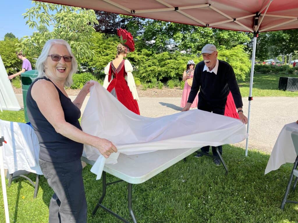 Vibrant outdoor scene at Oshawa Little Theatre with smiling people setting up for a performance.